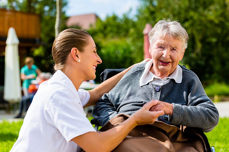 Eine Pflegerin und eine Seniorin sitzen gemeinsam im Garten und lachen